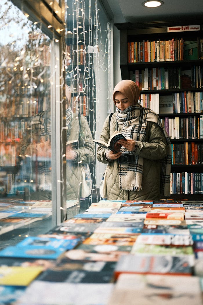 Press A woman in a hijab reads a book in a cozy bookstore with warm lighting.